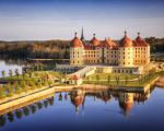 Luftaufnahme von Schloss Moritzburg im Frühling, umgeben von Wasser und Parkanlagen mit Spiegelung im See