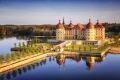 Luftaufnahme von Schloss Moritzburg im Frühling, umgeben von Wasser und Parkanlagen mit Spiegelung im See