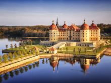 Luftaufnahme von Schloss Moritzburg im Frühling, umgeben von Wasser und Parkanlagen mit Spiegelung im See