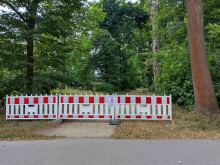 Gesperrter Parkweg im Großen Garten Dresden mit rot-weißer Absperrung und Warnschild vor herabfallenden Ästen, umgeben von dichtem Baumbestand