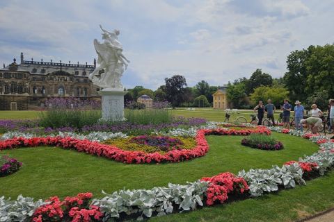 Gruppe von Menschen mit Fahrrädern während einer Stadtführung im Großen Garten Dresden, vor barockem Palais und Blumenbeeten mit Statue