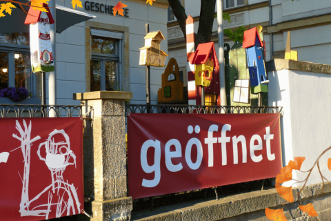 Bunte Vogelhäuschen und Herbstlicht in der Dresdner Neustadt Herbstliches Straßenszene in der Dresdner Neustadt mit bunten Vogelhäuschen, orangen Herbstblättern und einem roten Banner mit der Aufschrift „geöffnet“ an einem Zaun vor einem Geschäft
